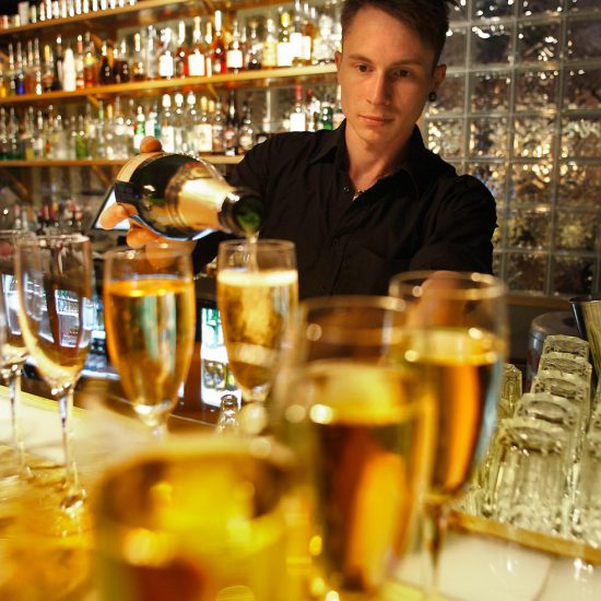 servitör häller i champagne i glas med en synligt barskåp i bakgrunden.