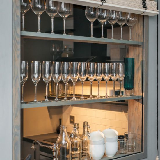 Smart förvaringslösning för glas i ett litet utrymme där väggen används som förvaring och som fönster mellan två mindre ytor.